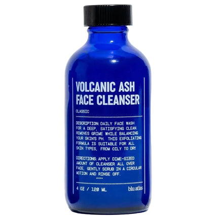 A cobalt blue glass bottle of Alana's 'Volcanic Ash Face Cleanser' with a black cap, centered against a light gray background.