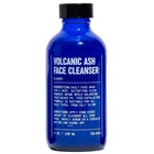 A cobalt blue glass bottle of Alana's 'Volcanic Ash Face Cleanser' with a black cap, centered against a light gray background.